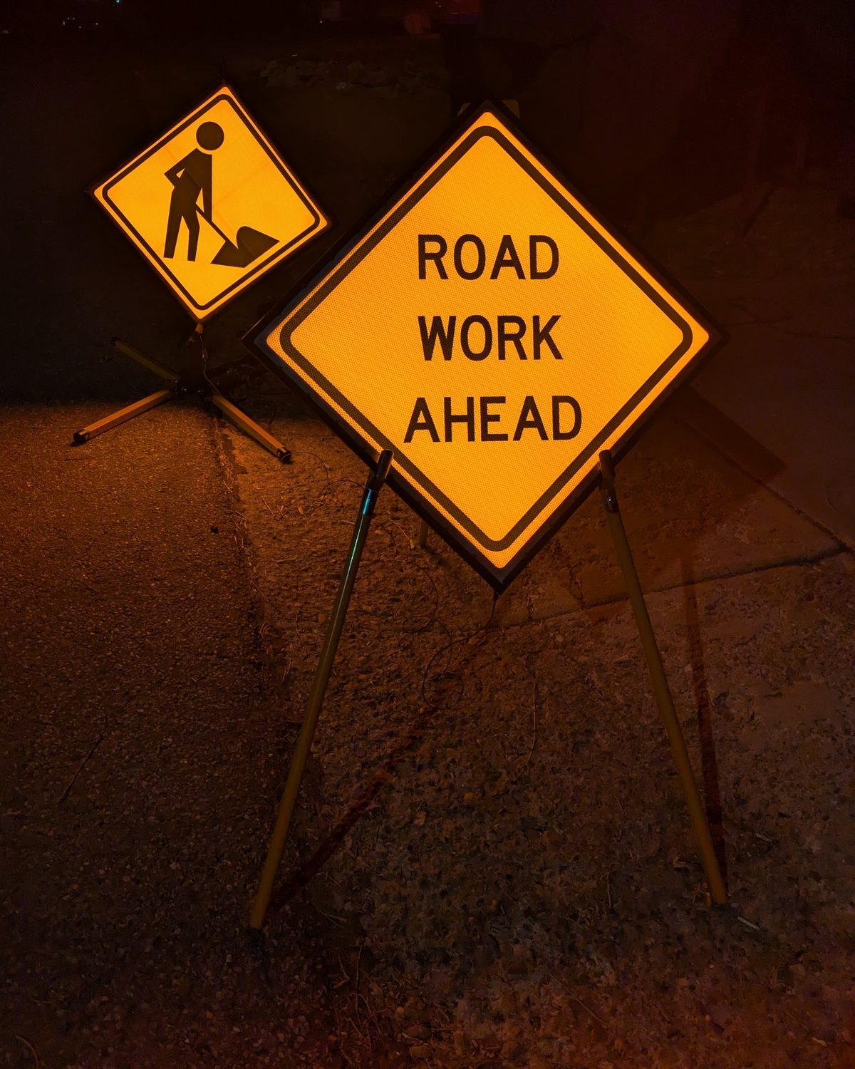 Two early RADROAD-APEX prototype work zone signs, ROAD WORK AHEAD and a worker symbol, internally illuminated at night