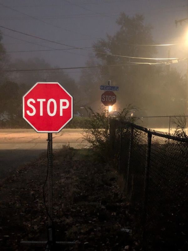 APEX I Alpha Unit R1-1 STOP sign, lit, at the corner in heavy fog under a streetlight